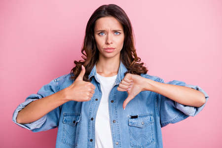 Photo of upset young woman show thumb up thumb down bad mood isolated on pastel pink color backgroundの写真素材