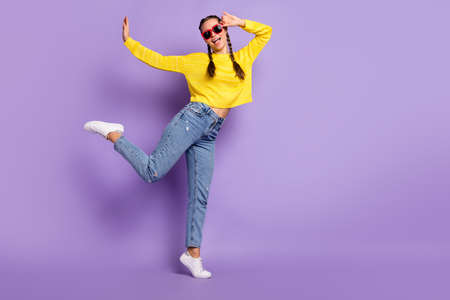Full body portrait of cheerful nice young girl dancing hand touch sunglass raise leg isolated on purple color backgroundの写真素材