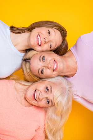 Vertical photo of nice optimistic three woman grand mom daughter wear pastel cloth isolated on yellow color backgroundの写真素材