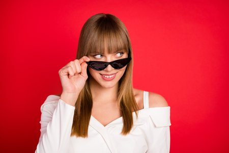 Photo of young woman happy positive smile hand touch glasses look empty space isolated over red color backgroundの写真素材