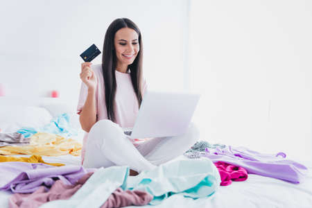 Photo of pretty sweet young woman nightwear sitting bed typing modern gadget bank card choosing new dress inside indoors home roomの写真素材