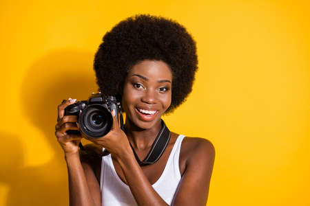 Close-up portrait of lovely cheery wavy-haired brunette girl holding in hands using digicam shooting isolated over bright yellow color backgroundの写真素材
