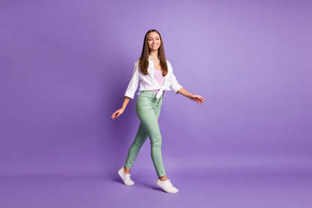 Full length photo of girl walk step wear sneakers trousers white shirt isolated violet color...