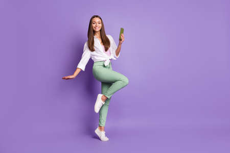 Photo of lady hold smartphone stand tiptoe girlish pose wear white shirt isolated purple color backgroundの写真素材