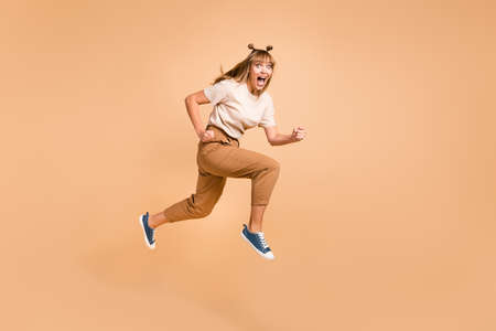 Full length profile photo of lady jump run open mouth yell wear t-shirt pants footwear isolated beige color backgroundの写真素材