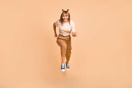 Full body photo of young girl happy positive smile jump up go run hurry sale isolated over beige color backgroundの写真素材
