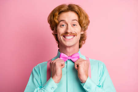 Photo of satisfied young person toothy smile hands fix bowtie look camera isolated on pink color backgroundの写真素材