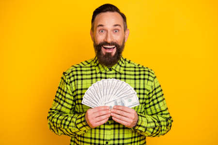 Photo of excited mature man happy positive smile hold money cash dollars banknotes rich isolated over yellow color backgroundの写真素材