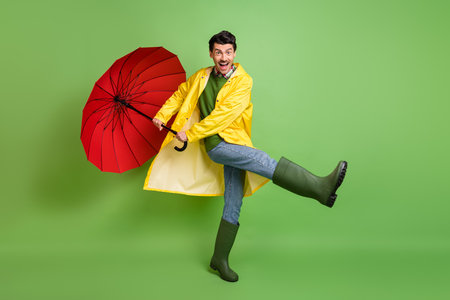 Full size photo of young happy excited good mood crazy man dancing with umbrella in hands isolated on green color backgroundの写真素材