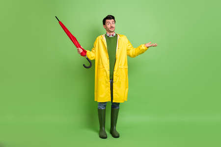 Full size photo of brunet clueless guy stand with umbrella wear cloak boots isolated on green color backgroundの写真素材