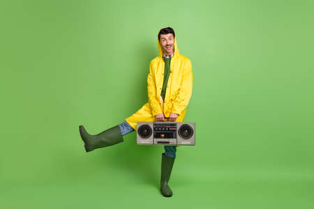 Full length body size view of attractive cheerful guy wearing raincoat having fun dancing sound isolated over bright green color backgroundの写真素材