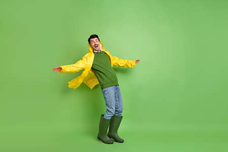 Full body profile side photo of young man surprised catch strong wind wear raincoat sweater isolated over green color backgroundの写真素材