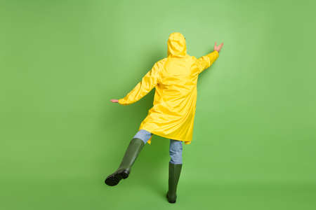 Back rear view photo of young man rainy weather wear raincoat try to catch umbrella incognito isolated over green color backgroundの写真素材