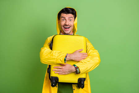 Photo of brunet optimistic guy hug bag wear cloak isolated on green color backgroundの写真素材