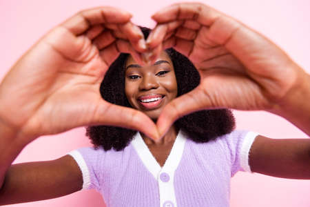 Close-up portrait of attractive cheerful wavy-haired girl showing heart shape affection amour isolated over pink pastel color backgroundの写真素材