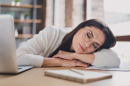 Photo of dreamy lady lay desk sleep workplace relax wear spectacles white pullover in living room home indoorsの写真素材