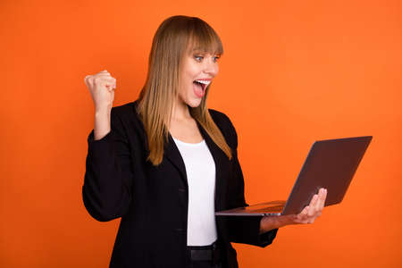 Portrait of attractive cheerful girl specialist using laptop rejoicing having fun luck isolated over bright orange color backgroundの写真素材