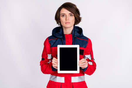 Photo of young serious beautiful woman paramedic demonstrate tablet touchscreen isolated on grey color backgroundの写真素材