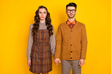 Portrait of attractive serious couple wearing checked uniform holding hands isolated over bright yellow color backgroundの写真素材