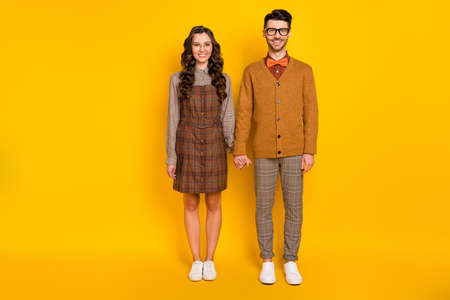 Full length body size view of attractive cheerful couple wearing uniform holding hands isolated over bright yellow color backgroundの写真素材