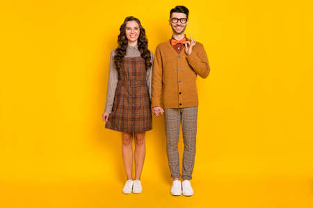 Full length body size view of attractive cheerful couple holding hands guy fixing bowtie isolated over bright yellow color backgroundの写真素材