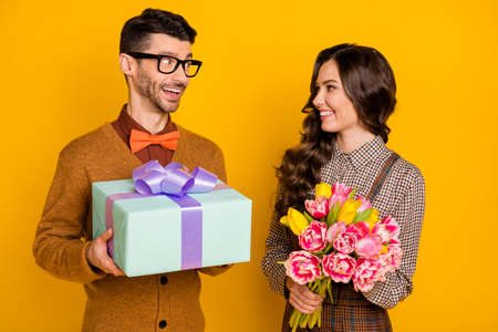 Photo of brown haired attractive couple give gift box hold flowers anniversary isolated on yellow color backgroundの写真素材