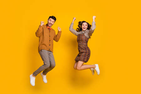 Full body photo of brown haired man and woman excited winner raise fists success jump isolated on yellow color backgroundの写真素材