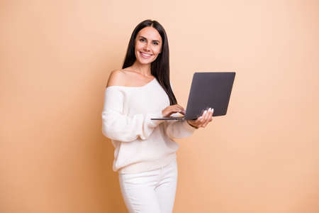 Photo of young woman programmer happy positive smile use laptop isolated over beige color backgroundの写真素材