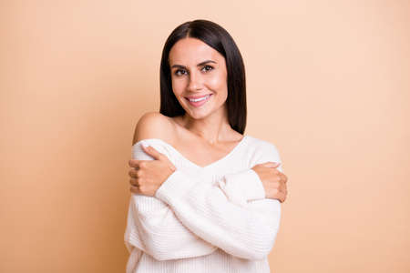 Photo of young attractive girl happy positive smile enjoy hug herself comfort cozy isolated over beige color backgroundの写真素材