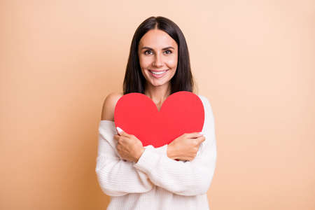 Photo of young girl happy positive smile hug big red heart cozy love feelings isolated over beige color backgroundの写真素材