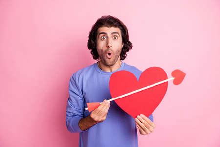 Portrait of impressed man open mouth hold red paper heart arrow purple pullover isolated on pink color backgroundの写真素材
