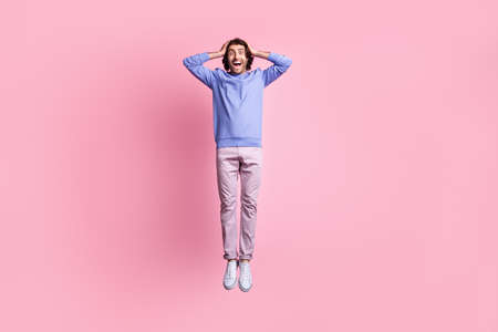 Full size photo of young handsome shocked amazed happy positive man hold hand head jump fly isolated on pink color backgroundの写真素材