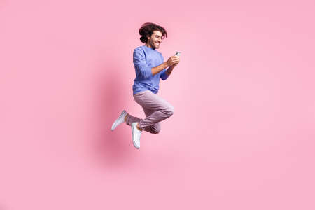 Full size photo of young happy smiling handsome positive man jump fly use smartphone isolated on pink color backgroundの写真素材