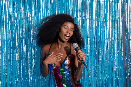 Portrait of attractive dreamy luxurious girl celebrity singing giving festal concert isolated over blue tinsel curtain backgroundの写真素材