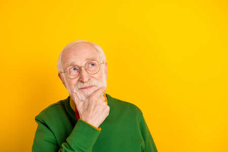 Photo of funny thoughtful mature man dressed pullover bow tie glasses arm chin looking empty space isolated yellow color backgroundの写真素材