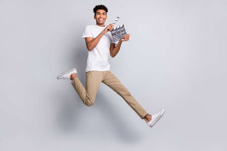 Photo of cheerful director guy jump hold clapboard run wear white t-shirt pants footwear isolated grey backgroundの写真素材