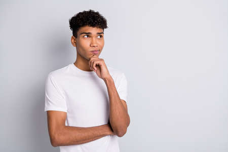 Photo of brunet strict curly guy stand hand chin look empty space wear white t-shirt isolated on grey color backgroundの写真素材