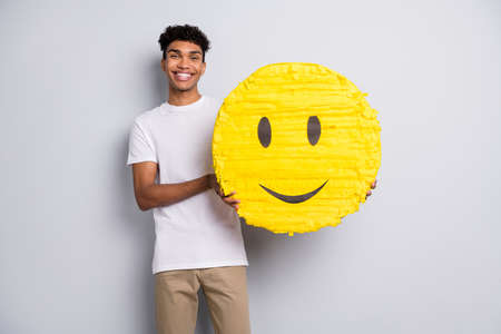 Photo of brunet optimistic curly guy hold pinata wear white t-shirt pants isolated on grey color backgroundの写真素材