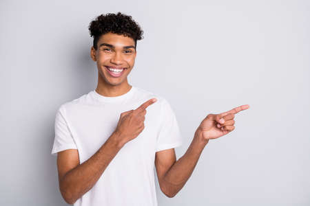 Photo of brunet optimistic curly funny guy point empty space wear white t-shirt isolated on grey color backgroundの写真素材