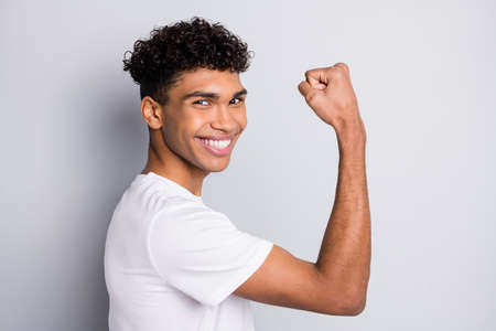 Profile portrait of brunet optimistic curly guy show muscle wear white t-shirt isolated on grey color backgroundの写真素材