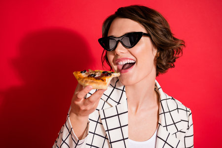 Photo of young attractive girl happy positive smile hungry eat fast food pizza isolated over red color backgroundの写真素材