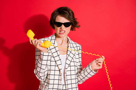 Photo of young woman unhappy mad angry talk answer cable telephone isolated over red color...