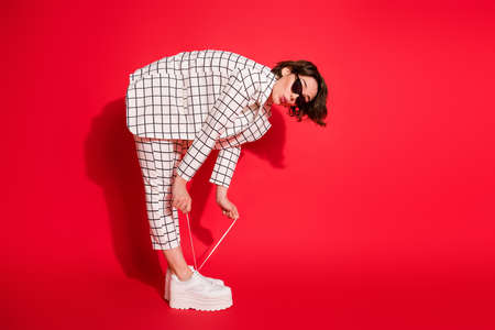 Full length body size profile side photo of young girl pouted lips bend shoe lace isolated over red color backgroundの写真素材