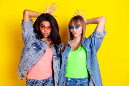 Portrait of two positive persons arms fingers make horns on head pouted lips isolated on yellow color backgroundの写真素材