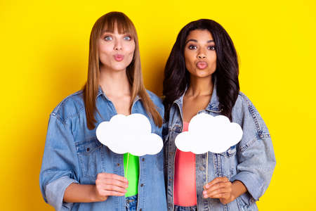 Portrait of attractive lovely ladies kiss lips hold cloud empty space shape wear denim isolated on yellow color backgroundの写真素材