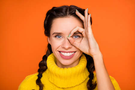 Portrait of brown hair optimistic girl show ok sign wear yellow sweater isolated on orange color backgroundの写真素材