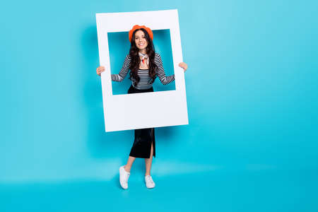 Full length portrait of positive young girl hands hold paper frame have good mood isolated on blue color backgroundの写真素材