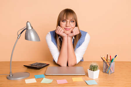 Photo portrait of woman in glasses sitting on table smiling near laptop isolated on pastel beige...