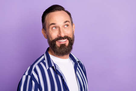 Photo of inspired thoughtful, mature man look empty space with toothy smile isolated over purple color backgroundの写真素材