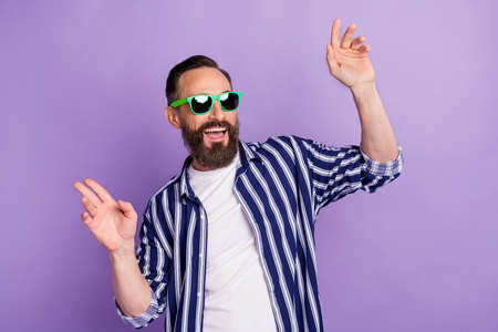 Photo of excited mature man in sunglasses raise hands up dance isolated over violet color background
